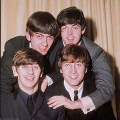 four young men in suits posing for a photo with their arms around each other's shoulders