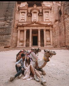 three people are sitting on the ground with a camel in front of a large building