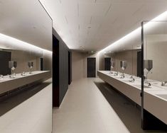 a long bathroom with sinks and mirrors in the middle of it, all lit up by lights