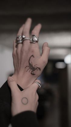 a woman's hand with a scorpion tattoo on it and two silver rings around her wrist