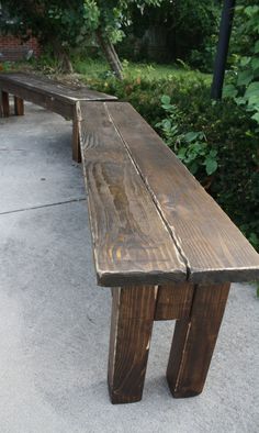 a wooden bench sitting on top of a cement floor next to bushes and trees in the background