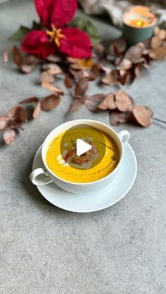 a white bowl filled with soup sitting on top of a table next to red flowers