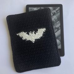 a black crocheted square with a white bat on it next to an ipad