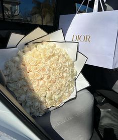 a bouquet of white roses sits in the back seat of a car, next to a dior bag