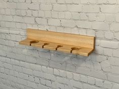 a wooden shelf on the side of a white brick wall with three pegs attached to it