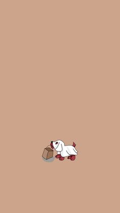 a white dog laying on top of a brown floor next to a brick wall with a box in it's mouth