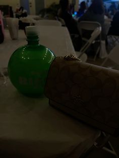 a green bottle sitting on top of a white table next to a brown handbag