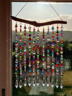 a wind chime hanging from a window in front of a tree branch with colorful beads on it