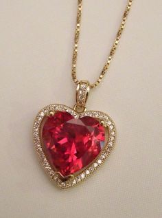 a red heart shaped necklace on a gold plated chain with white diamonds around it