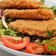 two fried chicken patties on top of a salad with tomatoes and lettuce