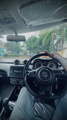 a man driving a car down a street next to a lush green forest filled with palm trees