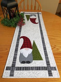 a christmas table runner with gnomes and trees on the top, sitting on a dining room table