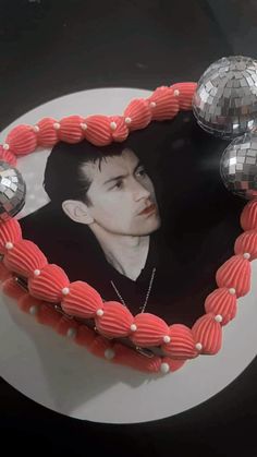 a cake shaped like a heart with a man's face in the middle and three disco balls around it