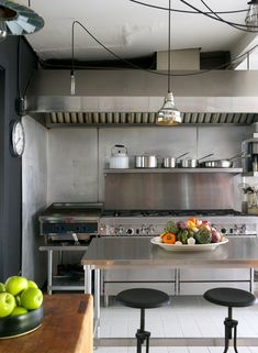 an industrial style kitchen with stainless steel appliances and fruit on the counter top, along with two stools