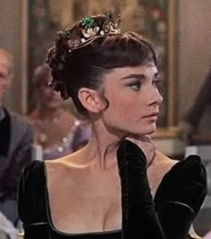 a woman wearing a black dress and a tiara in a room with other people