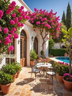 an outdoor dining area with potted plants and pink flowers on the wall, next to a swimming pool