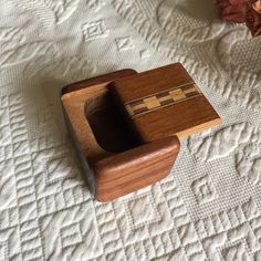 a small wooden box sitting on top of a white bed sheet with flowers in the background