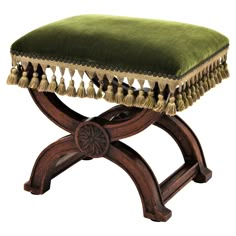 a green velvet foot stool with tassels on the top and bottom, sitting on a wooden stand