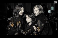 three women standing next to each other in black and gold jackets with the words sn written on them