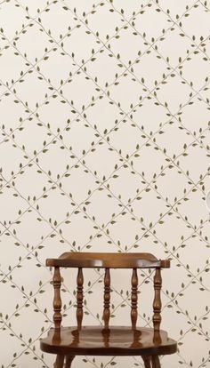 a wooden chair sitting in front of a wallpapered with small green leaves on it