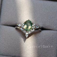 an engagement ring with a green stone surrounded by white diamonds on a gray velvet box