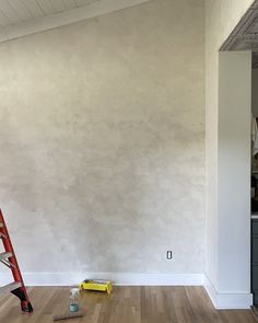 an empty room with a ladder, paint roller and other items on the floor in front of it