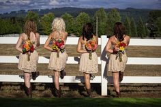 four women in short dresses are standing near a white fence and holding bouquets with their backs to the camera