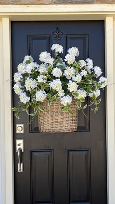 a basket filled with white flowers sitting on the front door to a black painted door