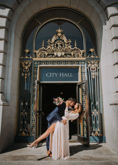 a man and woman kissing in front of a city hall entrance with their feet on each other