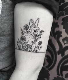 a small rabbit tattoo on the left inner forearm and arm, with daisies in the foreground