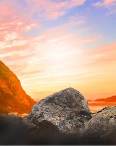 a rock sitting on top of a beach next to a body of water with a sunset in the background