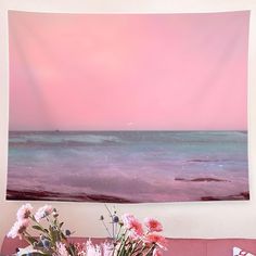 a pink and blue wall hanging over a couch with flowers in front of the ocean