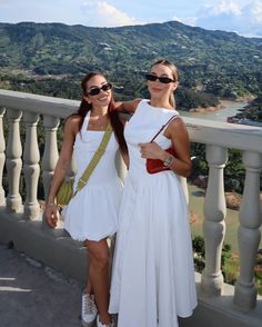 two women standing next to each other on top of a balcony with mountains in the background