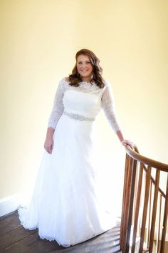 a woman in a white wedding dress standing on a wooden hand rail next to a yellow wall