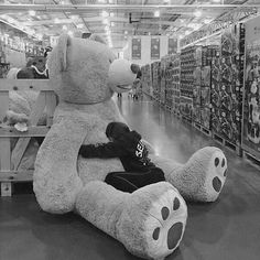 a large teddy bear sitting on top of a wooden shelf in a store filled with stuffed animals