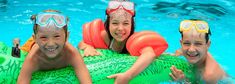 three children wearing goggles on inflatable rafts at the edge of a swimming pool