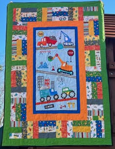 a quilted wall hanging on the side of a building with cars and trucks in it