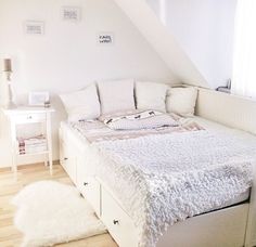 a white bed sitting in the middle of a bedroom under a slanted ceiling with windows