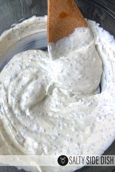 a wooden spoon in a bowl filled with white ranch dips and sauce on the side