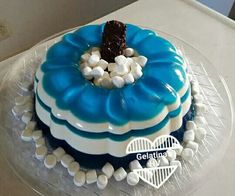 a blue and white cake with marshmallows on the top is sitting on a clear plate