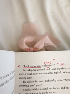 an open book with a pink bow on it's cover next to a white sheet