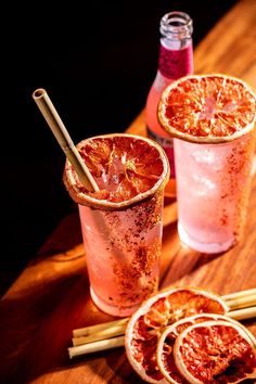 two glasses filled with blood oranges on top of a wooden table next to cinnamon sticks