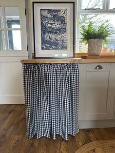 a kitchen counter with a blue and white checkered table cloth draped over it, in front of a window