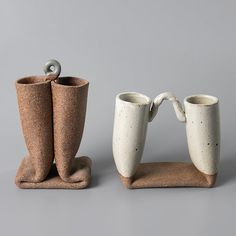 two white vases sitting next to each other on top of a brown stand with handles