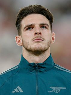 a close up of a soccer player wearing a green jacket and looking off to the side