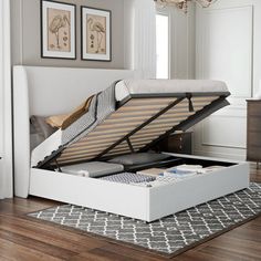 a white bed with an open box underneath it on the floor next to a rug