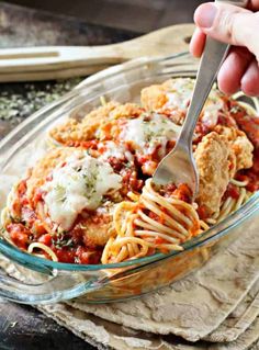 a person holding a spoon over a bowl of pasta with sauce and parmesan cheese