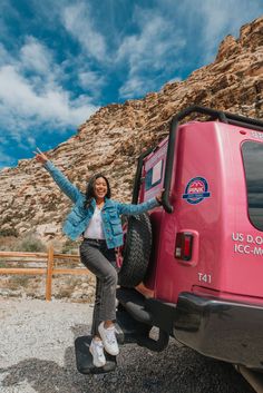 a woman standing in the back of a pink truck with her arms out and smiling