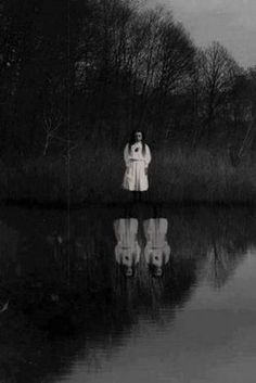 black and white photograph of a woman standing in front of a body of water surrounded by trees