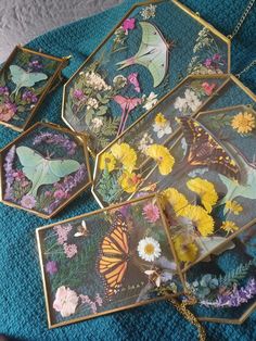 four small trays with butterflies and flowers on them sitting on a blue cloth covered table